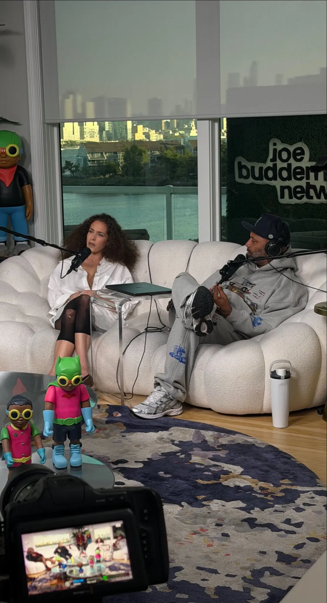 Maeta face à son hôte sur les fauteuils blancs du plateau du Joe Budden Network, micros en place, baie vitrée donnant sur la skyline